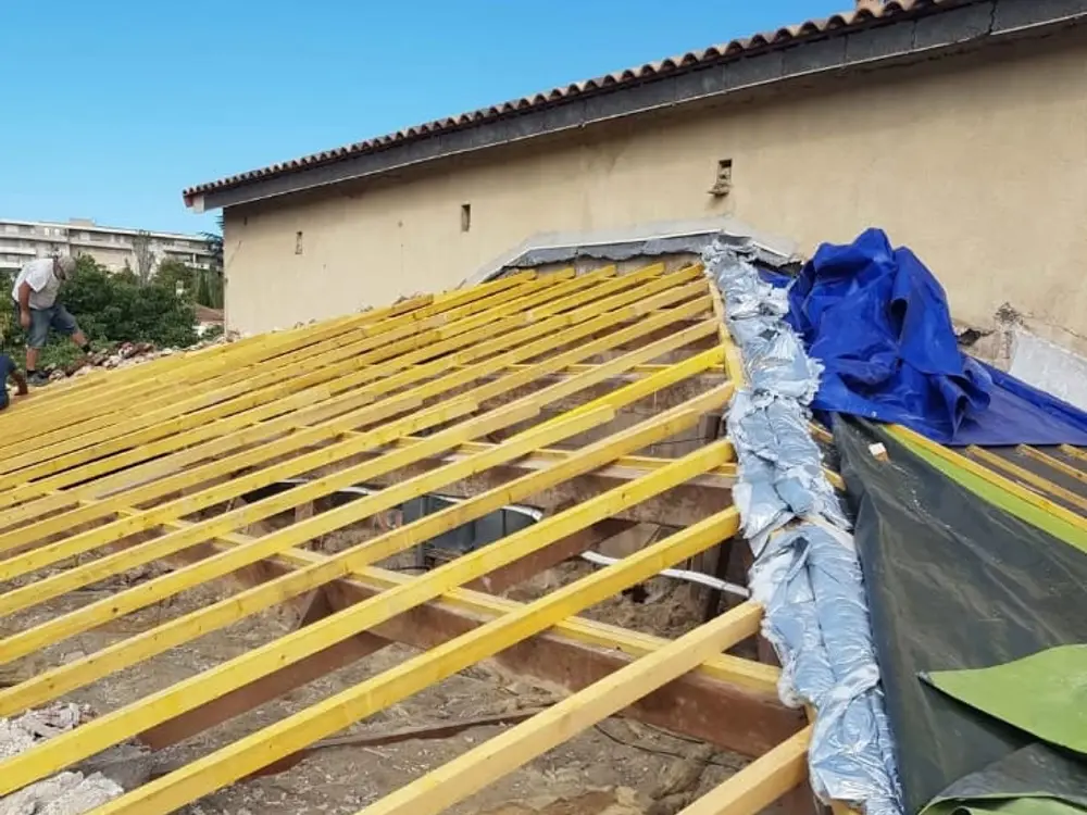 Solives et liteaunage en bois neuf posés sur une dalle, bâches de protection autour